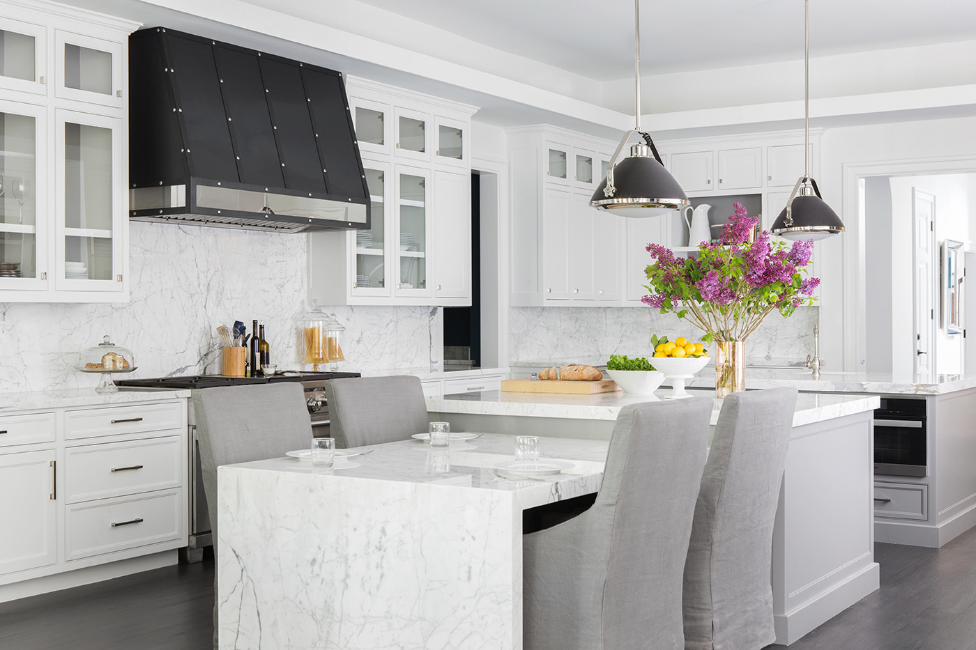 Adam Hunter designed kitchen with marble counters, a black hood, purple flowers and grey chairs.