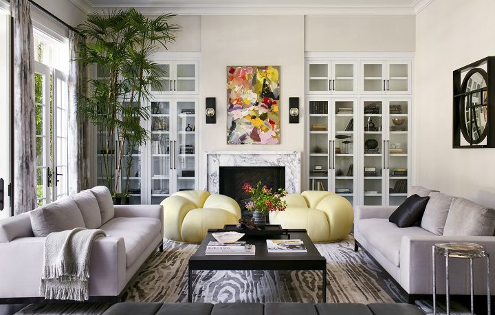 A living room designed by Adam Hunter that features two large yellow pouf chairs, his zebois rug, and two sofas.